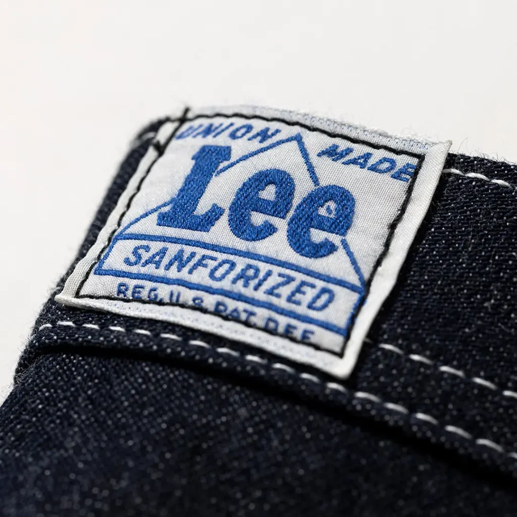 Close-up of the woven Lee Sanforized waistband label featuring blue lettering, Union Made branding, and vintage-inspired reproduction details on dark indigo denim