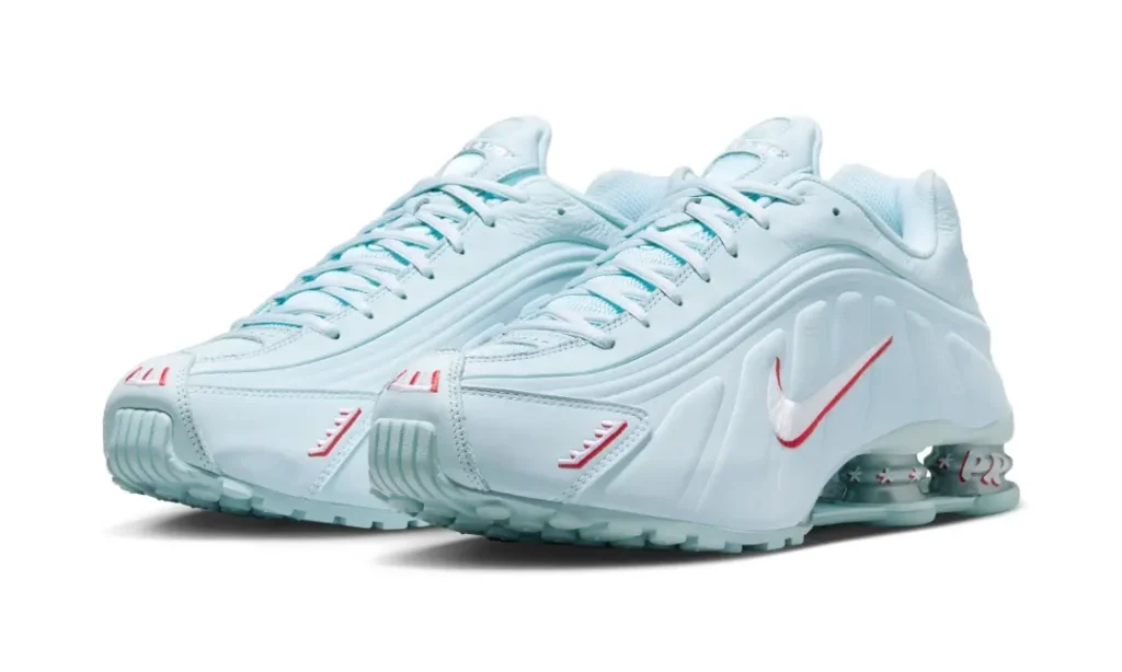 Nike Shox R4 Light Aqua shoe shown in an angled front view, featuring a pale blue leather upper, red embroidered accents, and signature Shox cushioning column