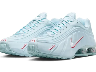 Nike Shox R4 Light Aqua shoe shown in an angled front view, featuring a pale blue leather upper, red embroidered accents, and signature Shox cushioning column