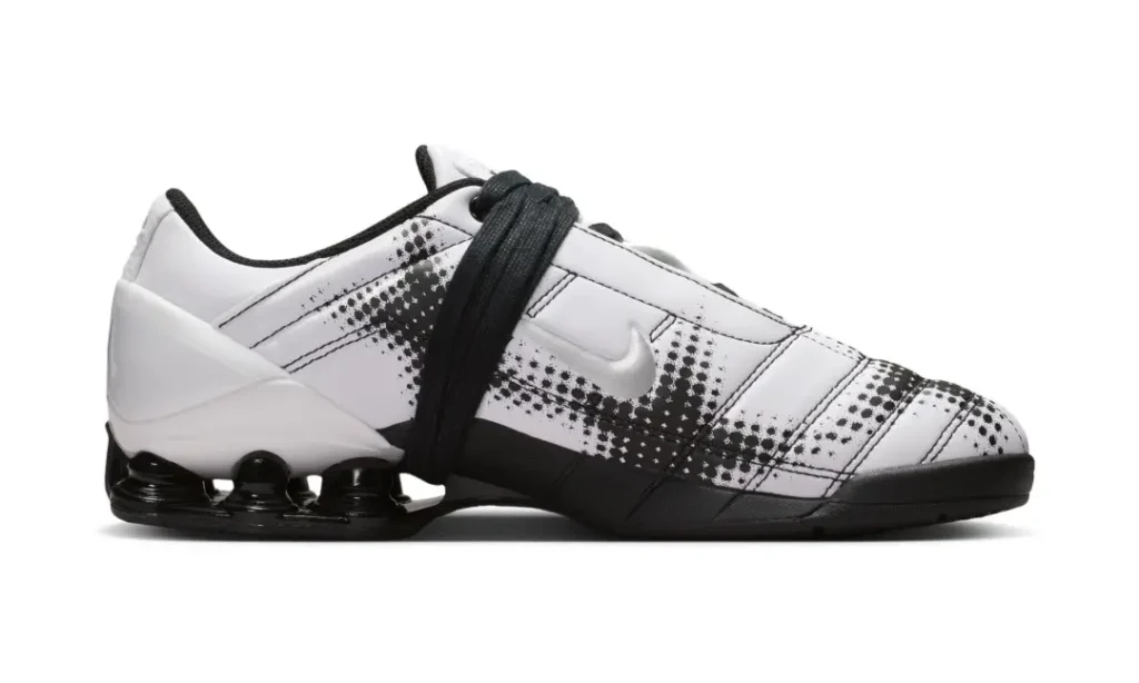 Lateral side view of the white sneaker emphasizing its clean monochrome palette, plaid-inspired print overlays, and glossy black Shox heel unit