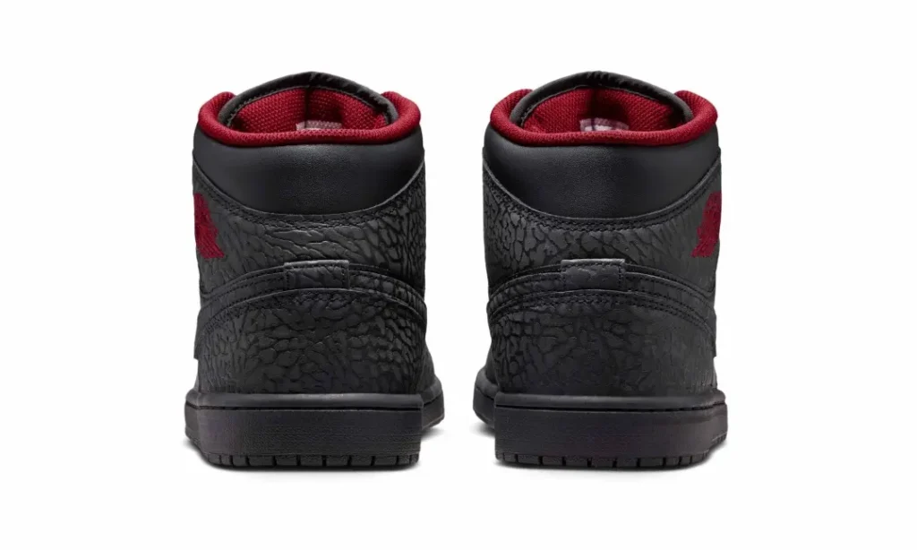 Rear view of the Air Jordan 1 Mid displaying textured elephant-print heel panels, padded black collars with crimson lining, embroidered red Wings logos, and black rubber mid