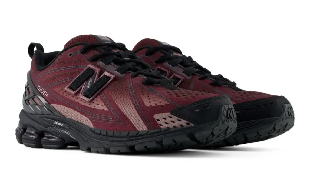 Angled product view of the New Balance 1906E in a rich burgundy and black colorway, showcasing breathable mesh construction, layered synthetic overlays, and the model’s distinctive segmented sole unit