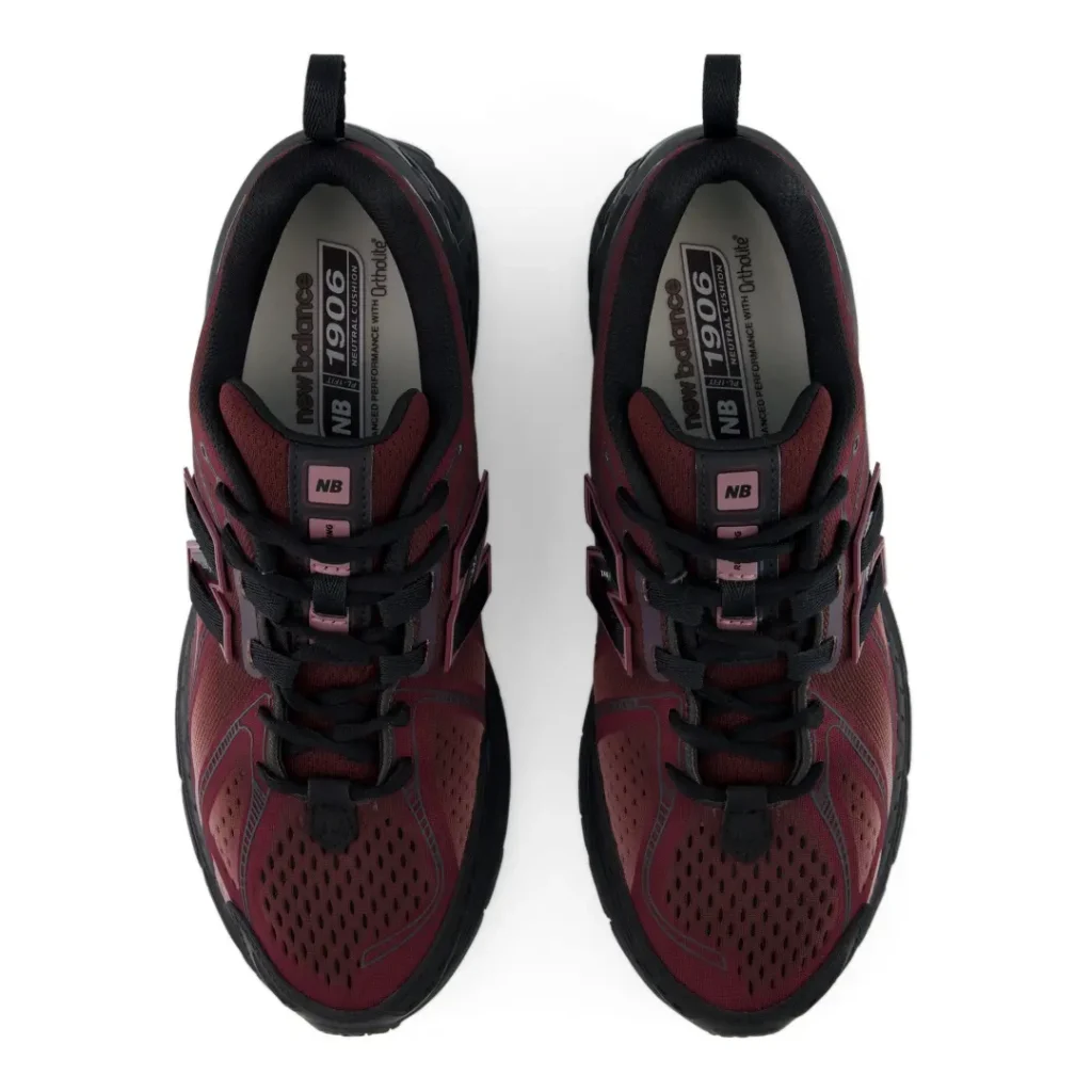 Top-down view of the New Balance 1906E revealing black laces, padded collars, perforated toe boxes, and branded insoles framed by the shoe dark red upper
