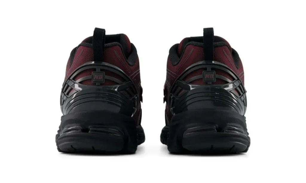 Rear view of the New Balance 1906E emphasizing the glossy black heel cage, pull tabs, cushioned heel pods, and the contrast between burgundy uppers and black tool