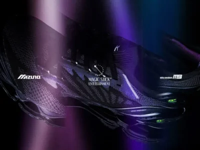 Close-up promotional image of the Mizuno Wave Prophecy LS collab with MAGIC STICK ENTERTAINMENT and mita shoe. The black performance shoe is shown against a dark background with dramatic purple light streaks, highlighting its engineered mesh upper, sculpted Wave Prophecy midsole, glossy heel counter, and collide branding for a futuristic, high-contrast show