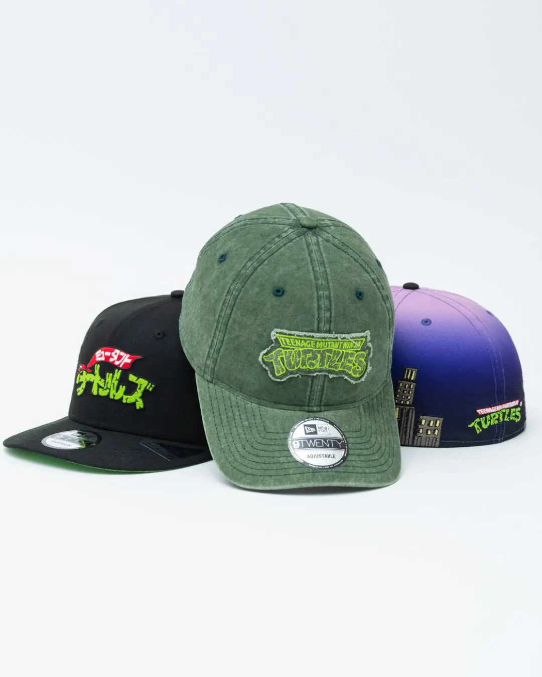 Three New Era Teenage Mutant Ninja Turtles caps arranged in a studio setting with a white backdrop. Centered is a washed olive-green 9TWENTY cap with a vintage-inspired TMNT logo patch, flanked by a black snapback with Japanese-style branding and a purple gradient fitted cap decorated with embroidered turtle characters and a city skyline motif