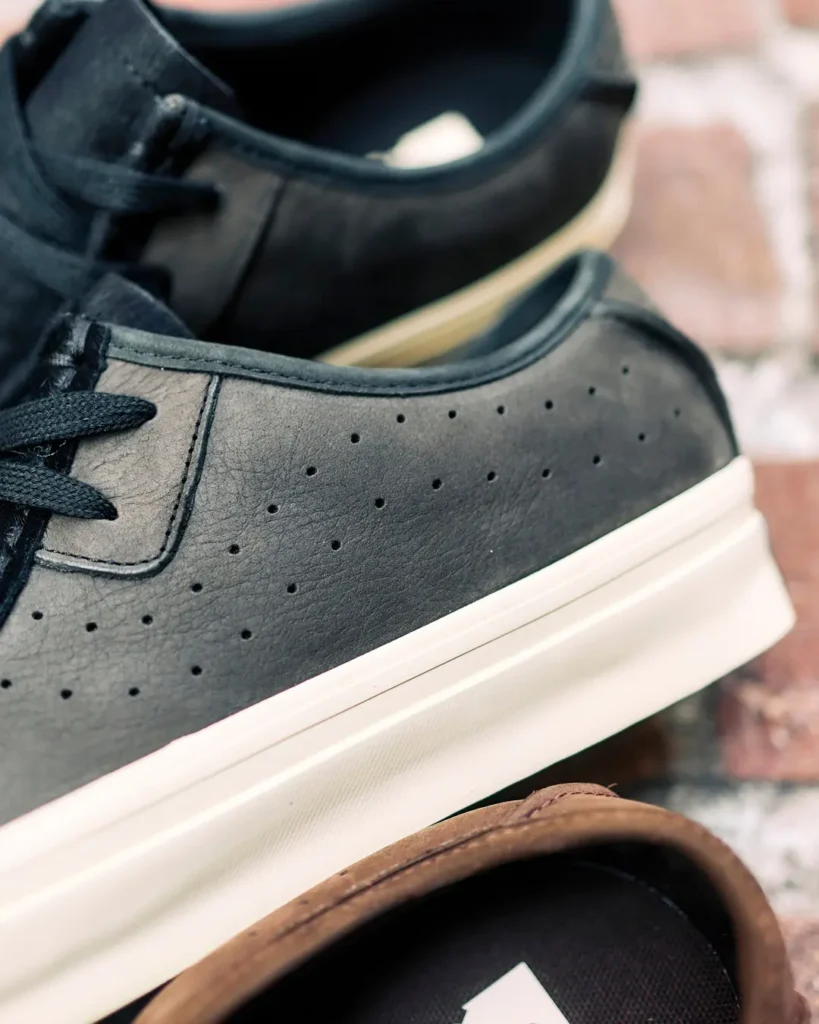 Close-up of the black sneaker’s lateral side, focusing on the perforated leather upper, tonal stitching, and slightly aged off-white sole. The image highlights the premium material finish and understated design