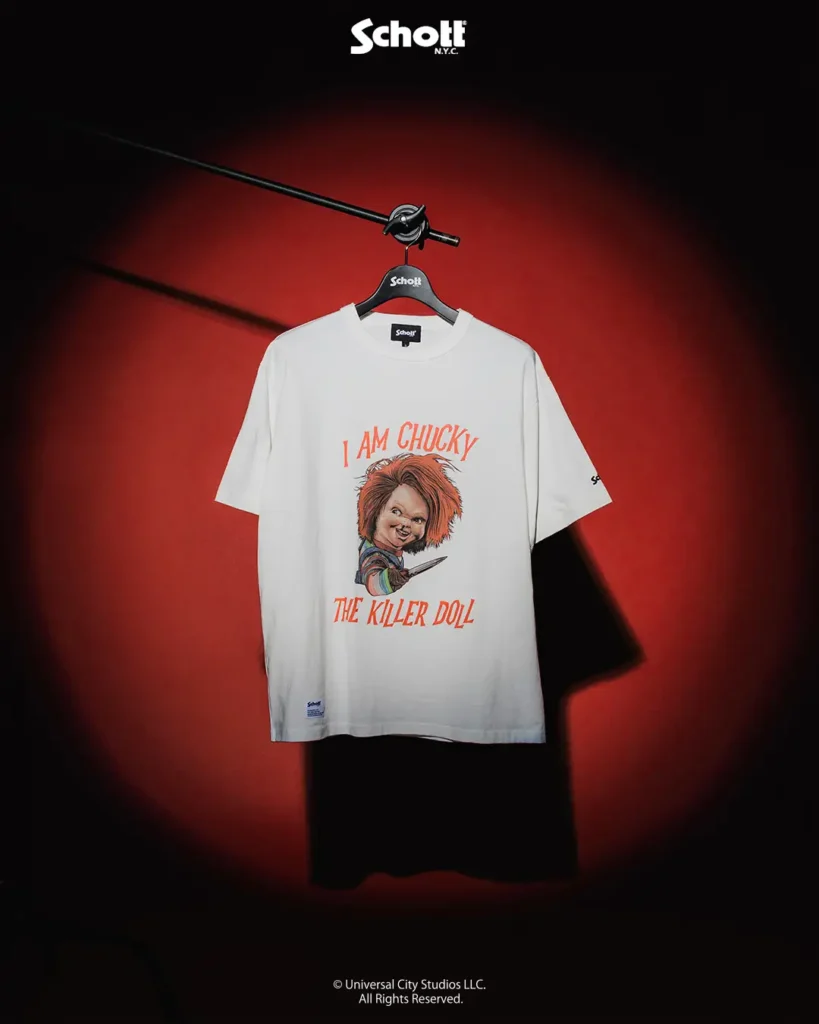 White graphic T-shirt from the Schott NYC x Chucky collaboration featuring an illustrated portrait of Chucky holding a knife with the slogan “I Am Chucky The Killer Doll” printed in bold orange lettering