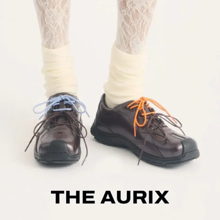 Model wears The Aurix leather shoes in a rich dark brown finish with contrasting light blue and orange laces. Styled with cream leg warmers and patterned lace tights against a clean studio backdrop, the chunky black outsole and reinforced toe emphasize the shoe's blend of utility, comfort, and contemporary fashion