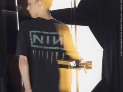 Model photographed in a studio wearing the Nine Inch Nails x monkey time collaboration T-shirt, featuring a distressed NIN logo graphic across the back with washed vintage detailing and oversized proportion