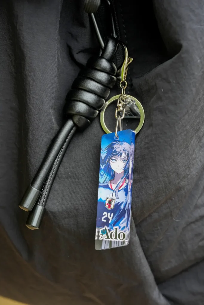 Ado collection acrylic keychain attached to a black bag, featuring anime artwork inspired by the Japan national team home jersey