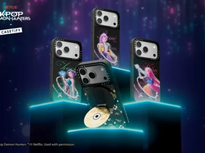 Four CASETiFY x Netflix KPop Demon Hunters smartphone cases displayed on illuminated podiums, each featuring stylized character artwork inspired by the animated film, with collectible accessories showcased against a neon purple concert-like backdrop