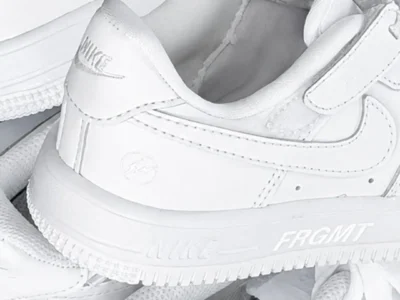 A close-up look at an all-white low-top Nike silhouette featuring subtle FRGMT branding on the midsole and a tonal lightning-bolt logo embossed near the heel. Clean leather panels, crisp stitching, and monochromatic detailing give the pair a minimalist, premium feel while highlighting Fragment Design’s understated approach to
