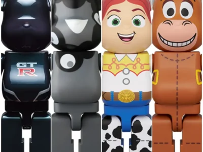 A composite image showcasing four collectible Bearbrick-style designer figures arranged side by side against a clean white background. From left to right: a glossy black figure inspired by the Nissan GT-R, featuring reflective surfaces, a GT-R logo on the torso, and bronze-toned foot accents; a minimalist black-and-gray figure decorated with abstract monochrome graphic shapes; a colorful figure modeled after Jessie from Toy Story, complete with red braided hair, a yellow western shirt, blue pants, and cow-print chaps; and a brown figure inspired by Bullseye, the horse from Toy Story, featuring a cheerful cartoon face, stitched detailing, and western saddle-inspired graphics. The lineup highlights a mix of automotive, contemporary art, and animated character influences within the iconic Bearbrick sil