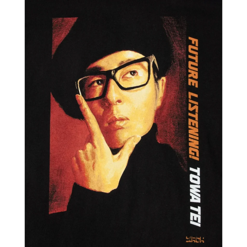 Close-up of the T-shirt's front graphic showing a warm-toned portrait of Towa Tei in a thoughtful pose, resting a finger against his cheek. Bold vertical lettering reading “FUTURE LISTENING! TOWA TEI” appears in orange and white beside the portrait, with a small orange logo at the bottom