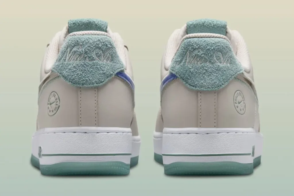 Back view highlighting textured aqua terry-cloth heel tabs embroidered with tonal Nike Air branding. The sail leather uppers are complemented by reflective silver Swooshes wrapping toward the heel and translucent icy-blue outsole edges. Circular Philadelphia-inspired emblems appear on the lateral heel panel