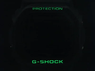thisisneverthat x G-SHOCK DW-6900TNT24-7DF in total darkness with signature green EL backlight illuminating "PROTECTION" above the dial and bold "G-SHOCK" below — the fourth collaboration’s subtle illuminated detail on the milky ivory Triple Graph model