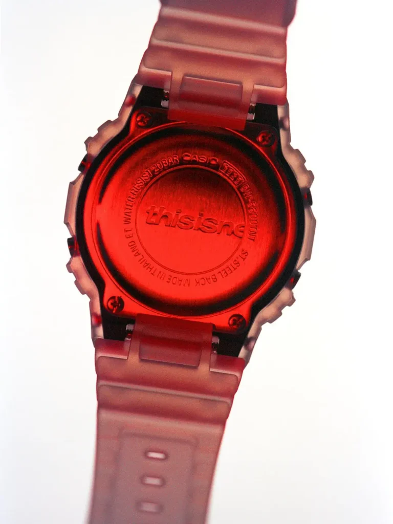 Rear view of the watch showcasing the stainless-steel caseback engraved with thisisneverthat branding. Dramatic red illumination reflects across the metal surface, emphasizing the collaborative detailing and durable construction