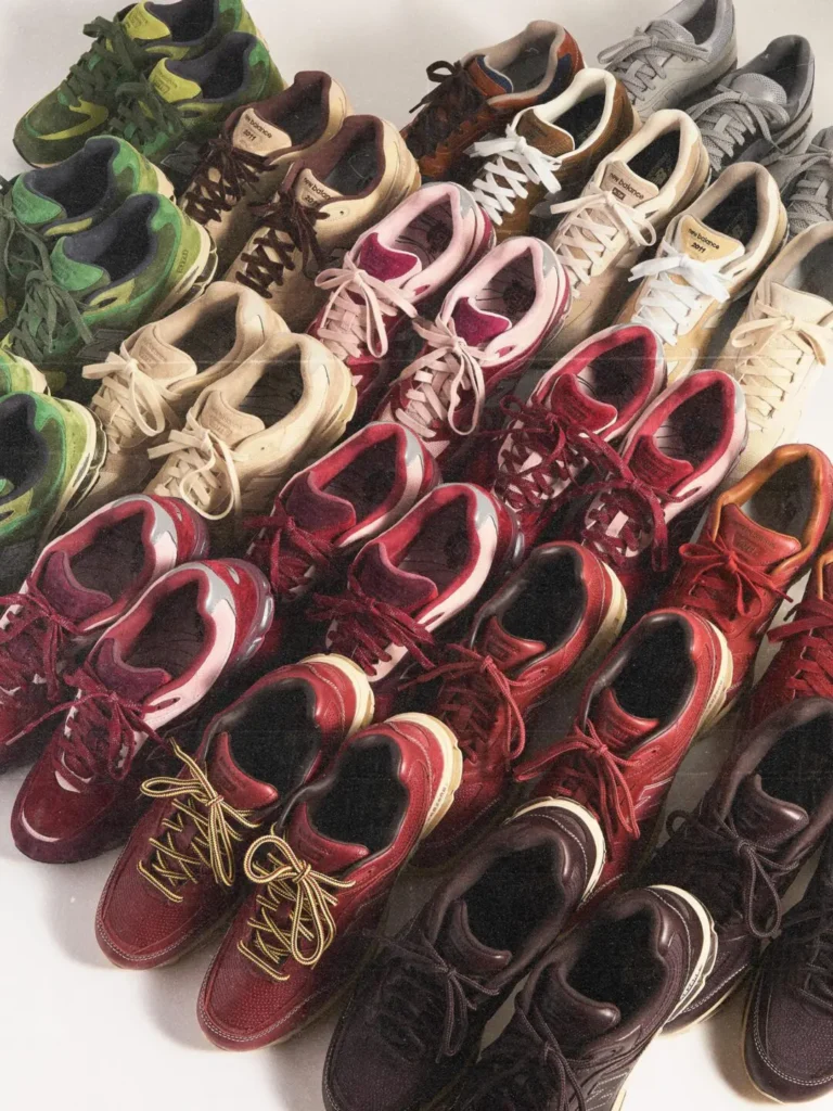 An assortment of completed and prototype New Balance sneakers is arranged across a tabletop. Various colorways in green, burgundy, cream, brown, grey, and pink showcase different material treatments and development stages, emphasizing the breadth of the collection’s design exploration