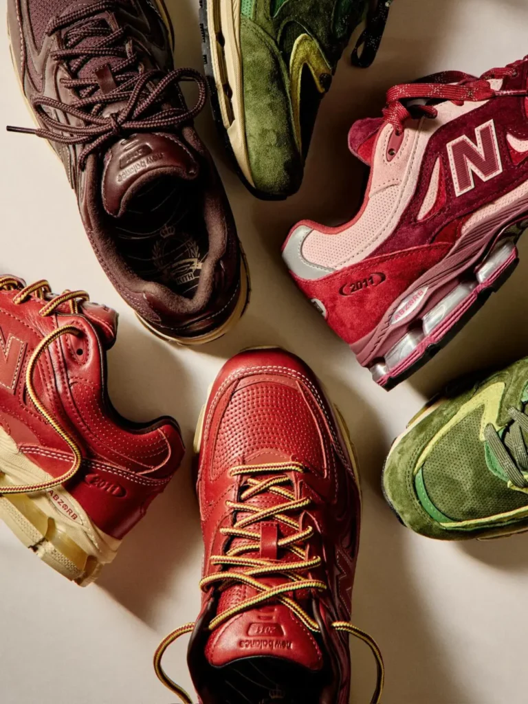Studio flat-lay photograph featuring multiple Kith x New Balance 2010 shoe arranged in a circular composition. Rich burgundy, dark brown, olive green, and wine-red colorways showcase premium suede and leather materials, highlighted by warm lighting and visible ABZORB cushioning detail