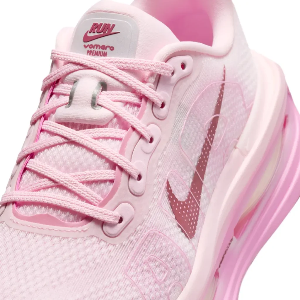 Close-up detail of the Nike Vomero Premium tongue branding, engineered mesh upper, and metallic pink Swoosh accent