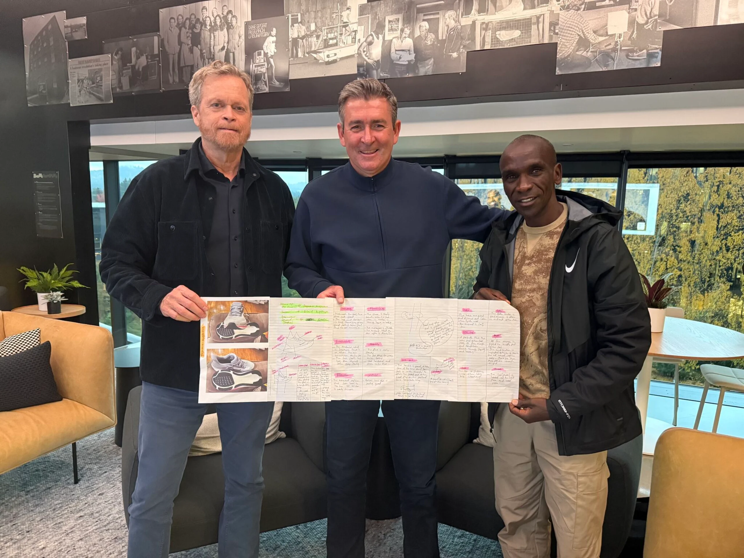 Phil McCartney stands alongside two colleagues inside Nike’s innovation campus, holding an athlete feedback and footwear development board featuring prototype images, design notes, and performance insights, highlighting the collaborative product creation process behind Nike running innovation