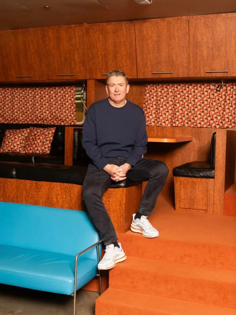 Phil McCartney sits inside a modern Nike workspace, wearing performance footwear while discussing the future of innovation, design, and product creation across the company