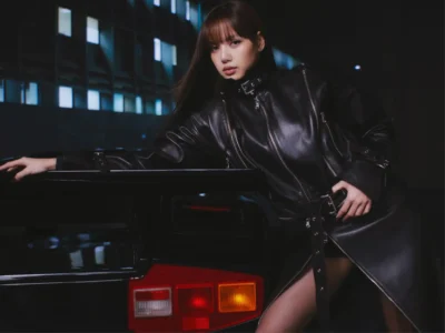 Lisa in black leather coat leaning against a vehicle at night, featuring an edgy urban fashion campaign aesthetic with illuminated city lights in the background