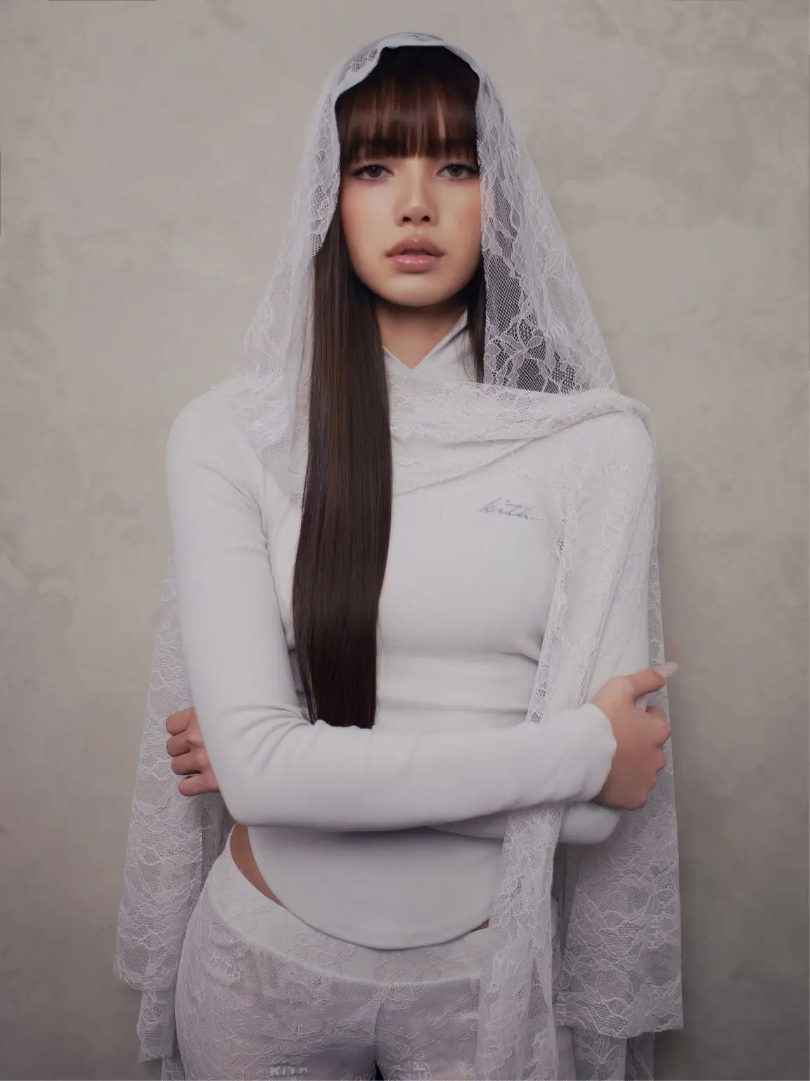 Lisa dressed in an all-white lace outfit with a sheer hooded veil, presenting a refined editorial portrait with elegant and romantic detail