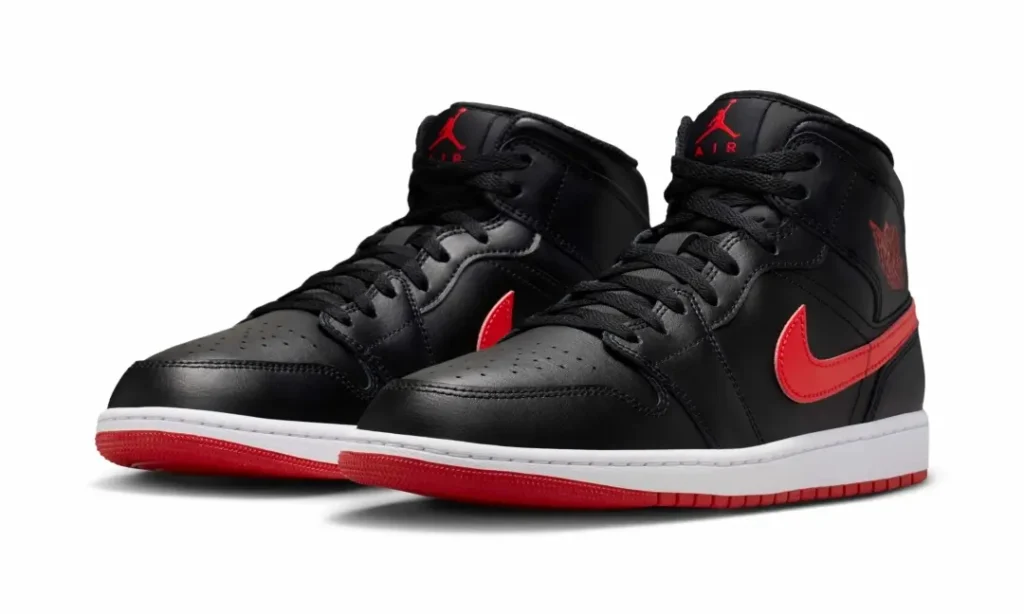 Pair of Air Jordan 1 Mid sneakers in black leather with bold red Swooshes, matching red outsoles, and white midsoles. The classic basketball silhouette is presented in a clean studio setting, highlighting its timeless tincture-blocking