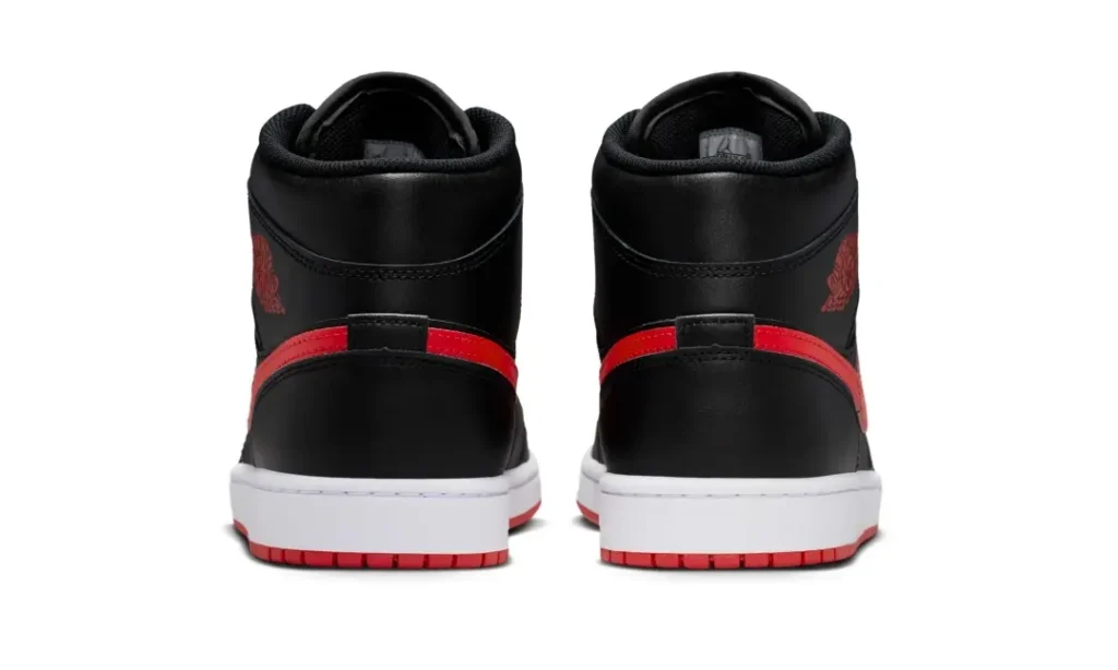 Rear view of the Air Jordan 1 Mid revealing black leather heel panels, red heel-wrap detailing connected to the Swoosh, and red rubber outsoles beneath crisp white mid