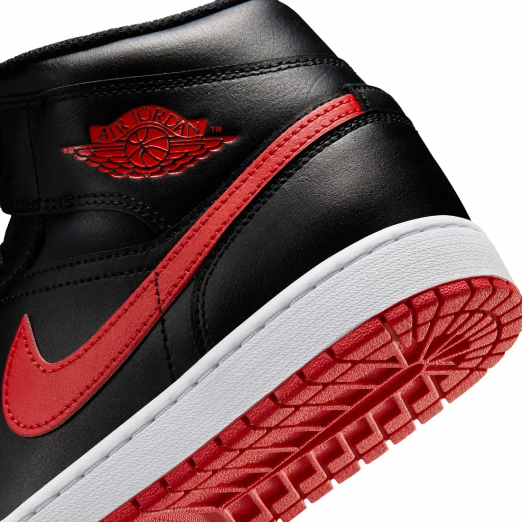 Macro shot of the Air Jordan 1 Mid’s heel area featuring the red Air Jordan Wings emblem, red leather Swoosh, textured white midsole, and vibrant red outsole tread pattern