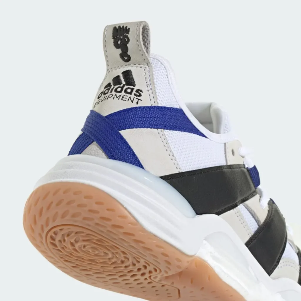 Heel close-up of the white Adidas Equipment sneaker showing embroidered Equipment branding, blue heel strap, textured gum outsole, and cushioned midsole