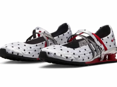 Pair of Nike Shox Mary Jane sneakers in white satin with black polka dots, photographed against a light gray studio background. The design features metallic silver crossover straps, red elastic detailing, chrome heel accents, and signature red Shox cushioning column