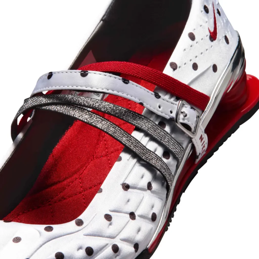 Close-up of the Nike Shox Mary Jane midfoot area highlighting metallic silver crossover straps, adjustable buckle hardware, red elastic support bands, and textured white satin material covered in black polka dots