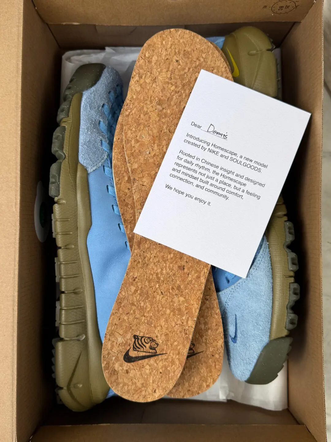 Inside the shoebox, the shoe are displayed alongside cork insoles and a printed welcome card. The presentation highlights the premium packaging, collaborative branding, and natural-material inspiration behind the Homescape project