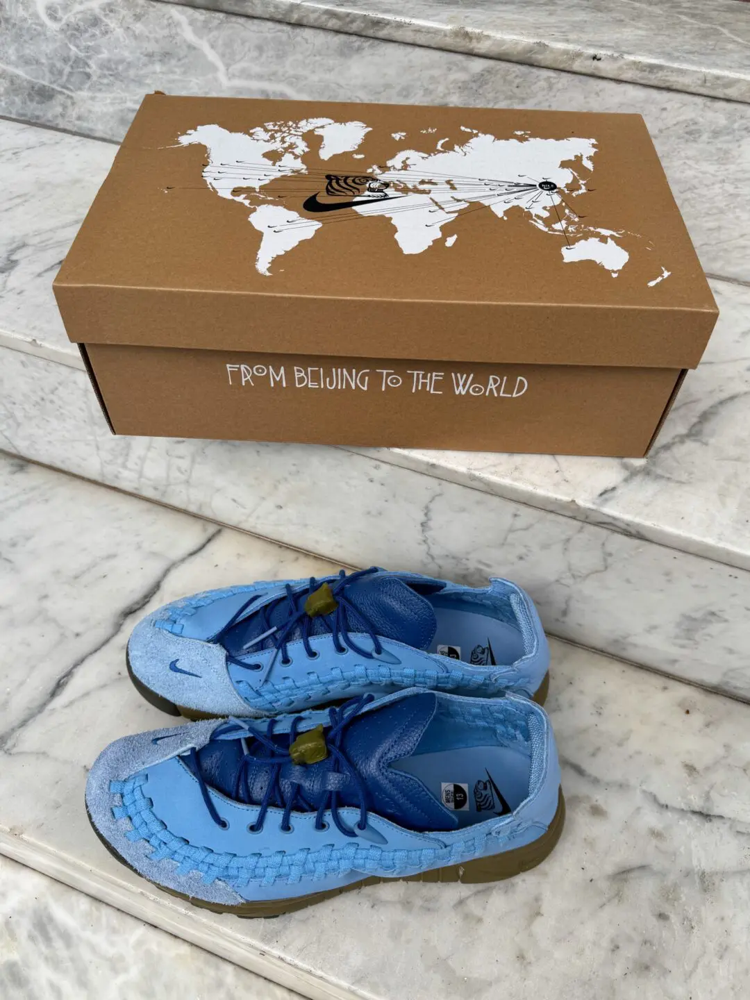 The special-edition brown shoebox features a world map graphic with travel-route illustrations and collaborative Nike x SOULGOODS branding. “FROM BEIJING TO THE WORLD” is printed across the front, emphasizing the collection’s global design nar
