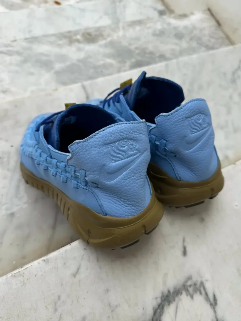 Rear three-quarter view of the Nike x SOULGOODS Homescape. The tumbled leather heel panels feature embossed collaborative graphics above subtle Swoosh branding, while the olive-green sole wraps around the heel for a sturdy, grounded look