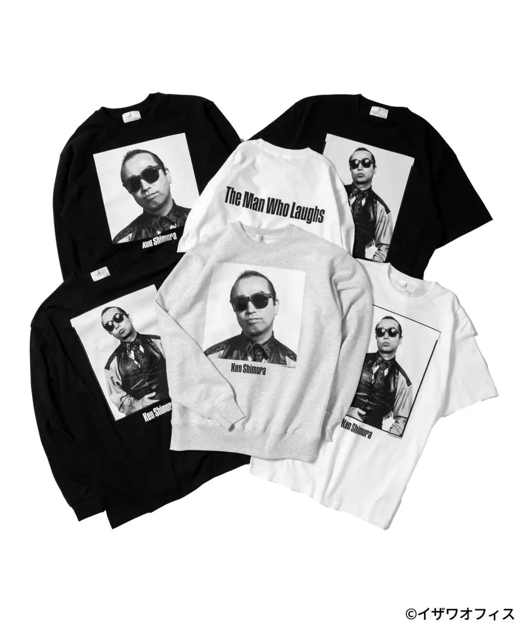 Flat lay showcasing the full Ken Shimura apparel collection, including black and white T-shirts, black and gray crewneck sweatshirts, and long-sleeve shirts. Each piece features archival black-and-white portrait photography of Ken Shimura, with select garments displaying bold back graphics reading "The Man Who Laughs" or "It's all right." The monochrome presentation highlights the tribute collection's clean, min show