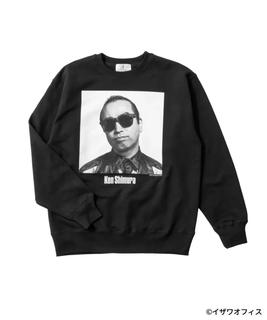 Black crewneck sweatshirt featuring a large black-and-white portrait of Ken Shimura wearing dark sunglasses. His name is printed beneath the image in bold lettering, creating a minimalist memorial-inspired graphic on a heavyweight cotton sweatshirt with ribbed cuffs and hem