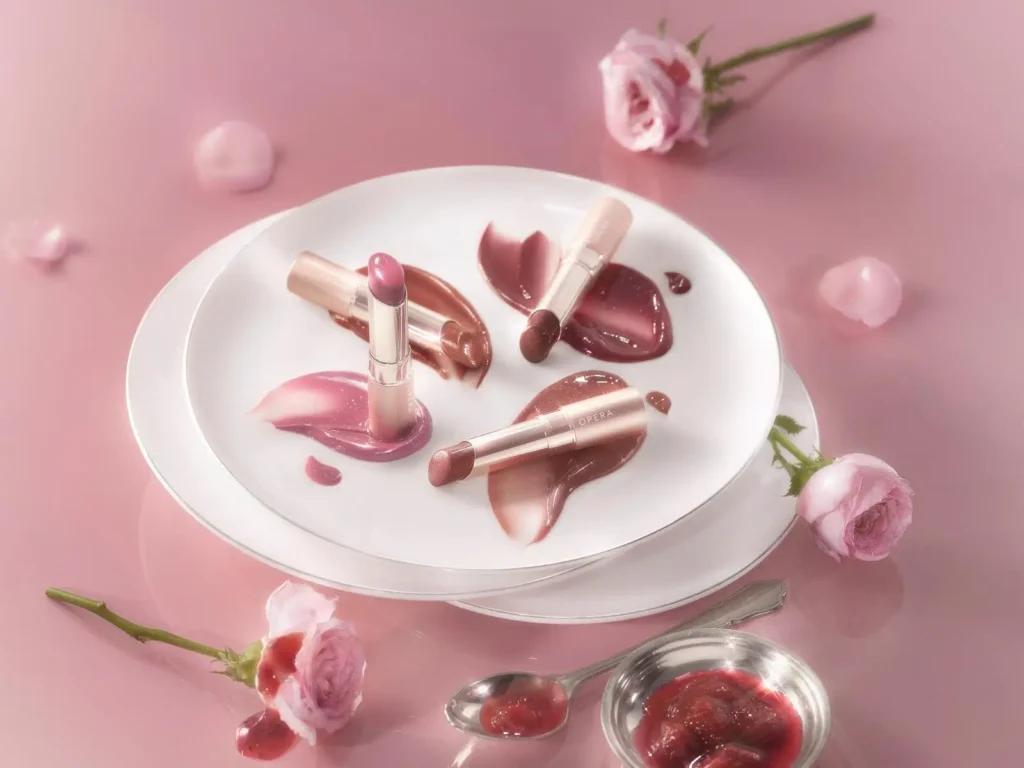 OPERA 26 Autumn Cosmetics Rose Jam and Sugar Glamer lip tints in brown and bordeaux shades displayed on white plate with rose petals and jam, pink background
