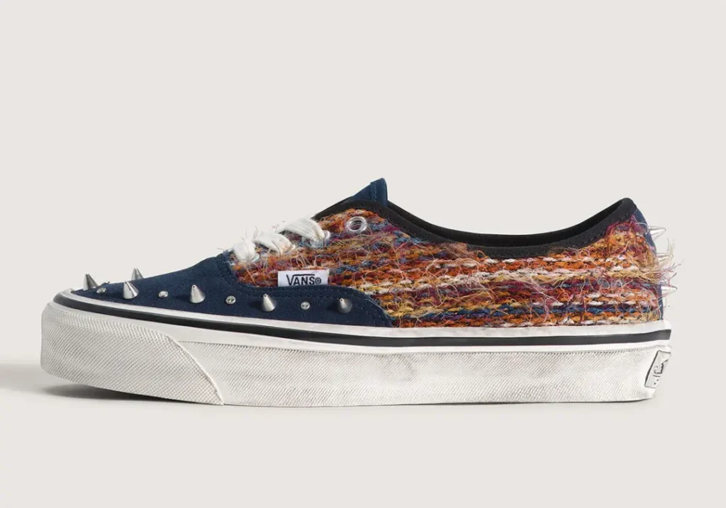 Side profile of the navy colorway. Deep blue suede overlays contrast with the multicolored woven upper, while silver spikes and crystal accents deliver a punk-inspired update to the classic Vans Era sil