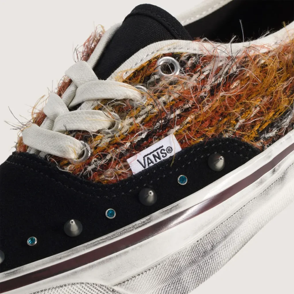 Close-up detail of the black colorway highlighting the richly textured woven upper, suede mudguard, Vans side tag, metallic cone studs, and small blue crystal accents. The worn midsole finish adds a vintage, DIY character