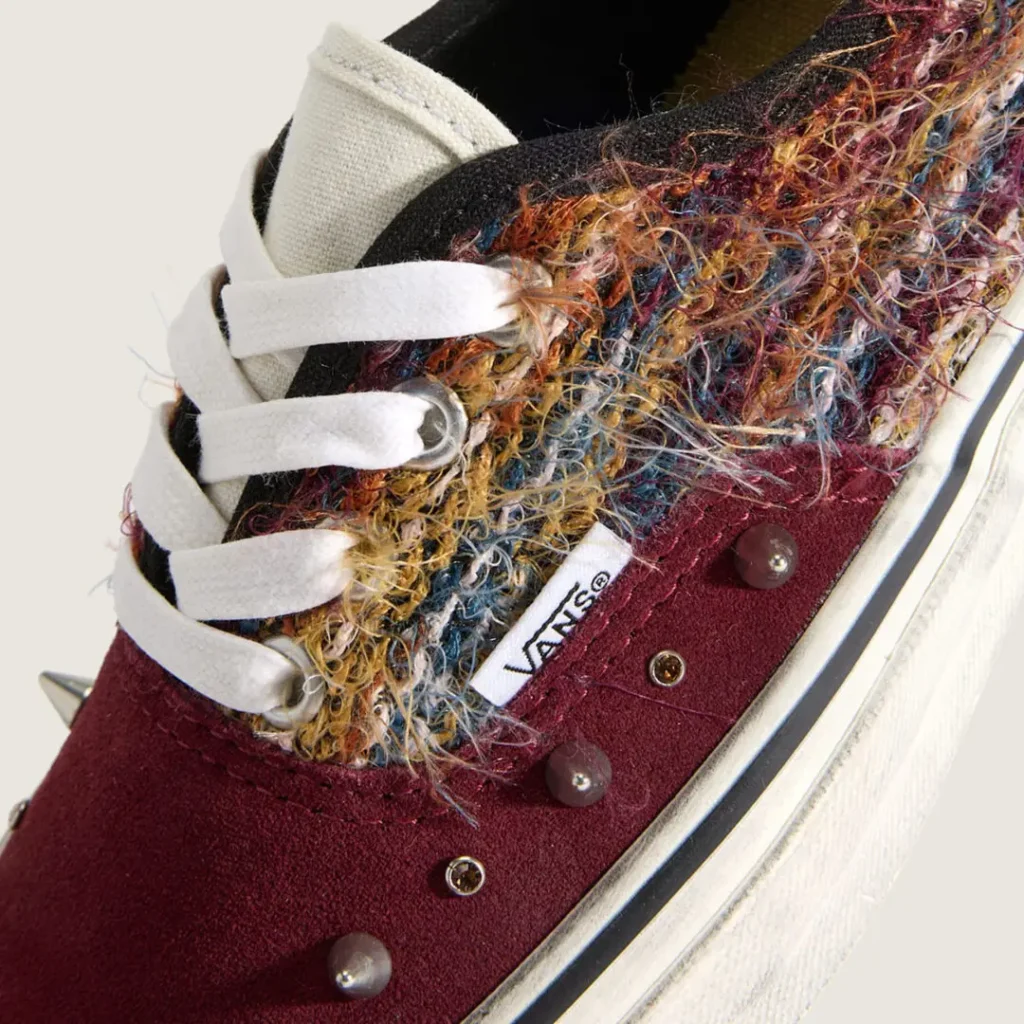 Close-up of the burgundy colorway. Rich wine-colored suede wraps the forefoot, paired with layered multicolored fibers, white laces, silver studs, and jewel-like accents that create a handcrafted, customized appearance