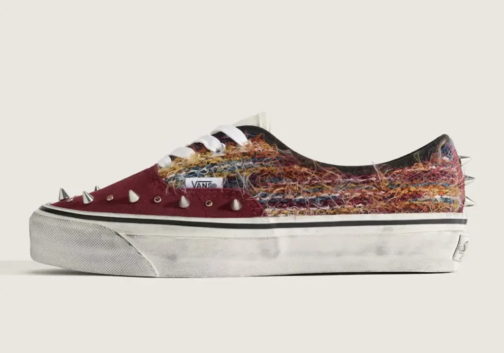 Side profile of the burgundy version highlighting the fuzzy woven textile upper, suede overlays, metallic cone spikes, and intentionally aged white foxing tape for a vintage skate-inspired look