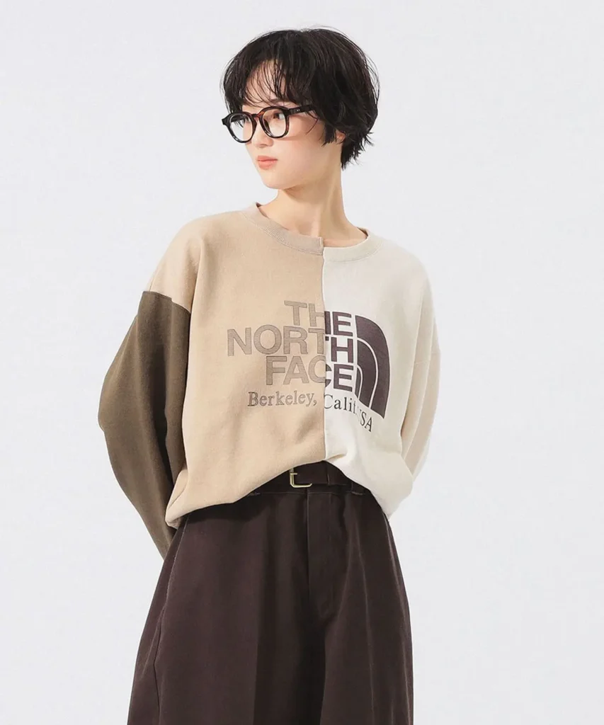 The North Face beige split-tone sweatshirt styled with tailored brown trousers, oversized fit, and heritage-inspired logo graphic