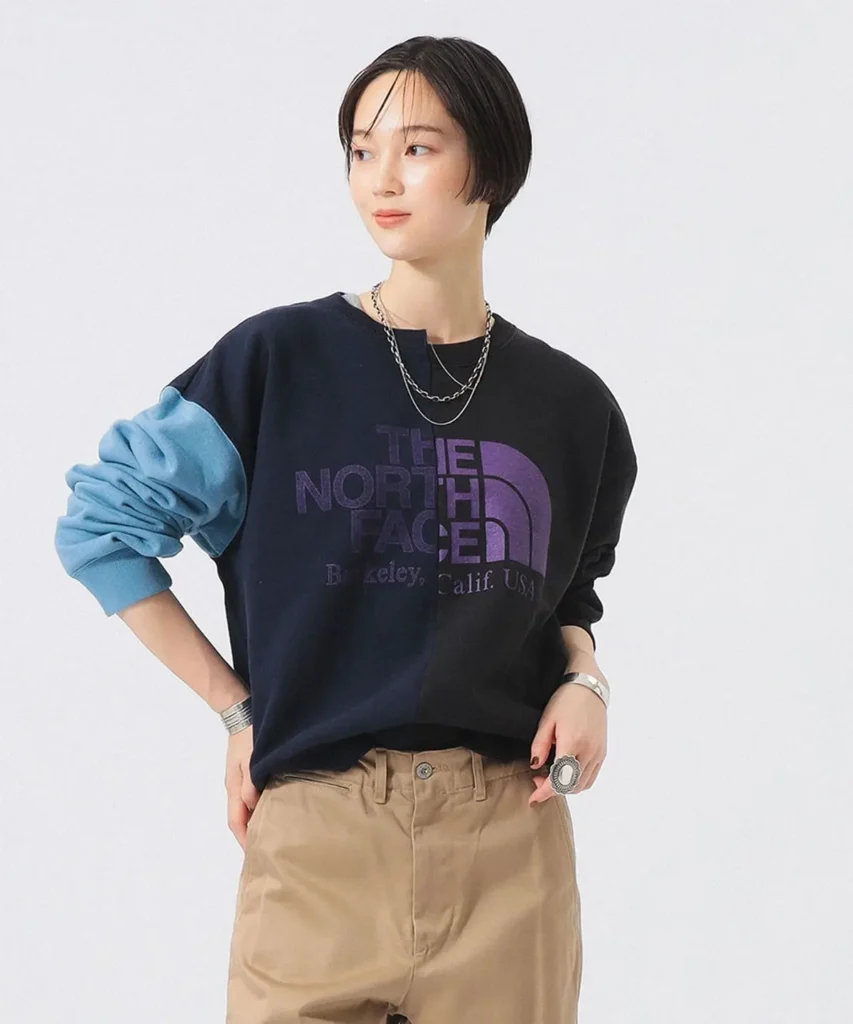 Model wearing navy and blue color-block The North Face sweatshirt with oversized logo graphic, layered jewelry, and relaxed style