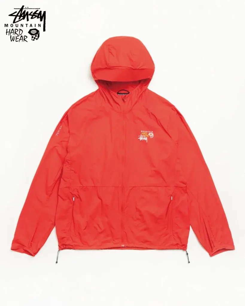 Bright orange hooded technical shell jacket from the Stüssy x Mountain Hardwear collaboration, featuring a full-zip front, adjustable hem, and lightweight outdoor construction