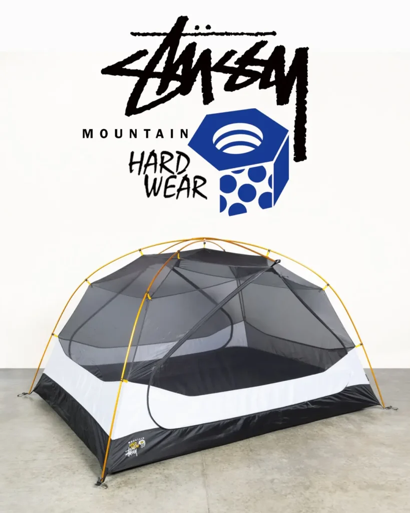 Freestanding Stüssy x Mountain Hardwear camping tent featuring black mesh walls, white lower panels, and bright yellow poles, displayed against a clean studio backdrop