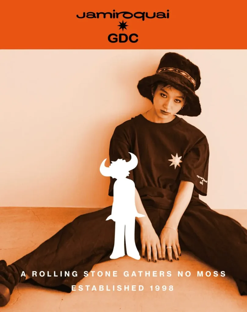 Detail photograph focusing on the sleeve branding of the black collaboration T-shirt. The cropped composition highlights the Jamiroquai and GDC logos printed near the cuff